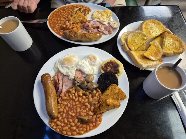 Fry-up with fried eggs, sausage, bacon, beans and black pudding, with toast and tea